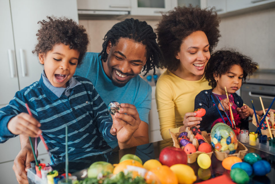 Young parents coloring animal eggs for Easter with their children