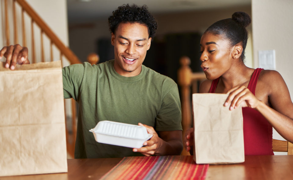 Couple sitting at table looking at food delivery at home