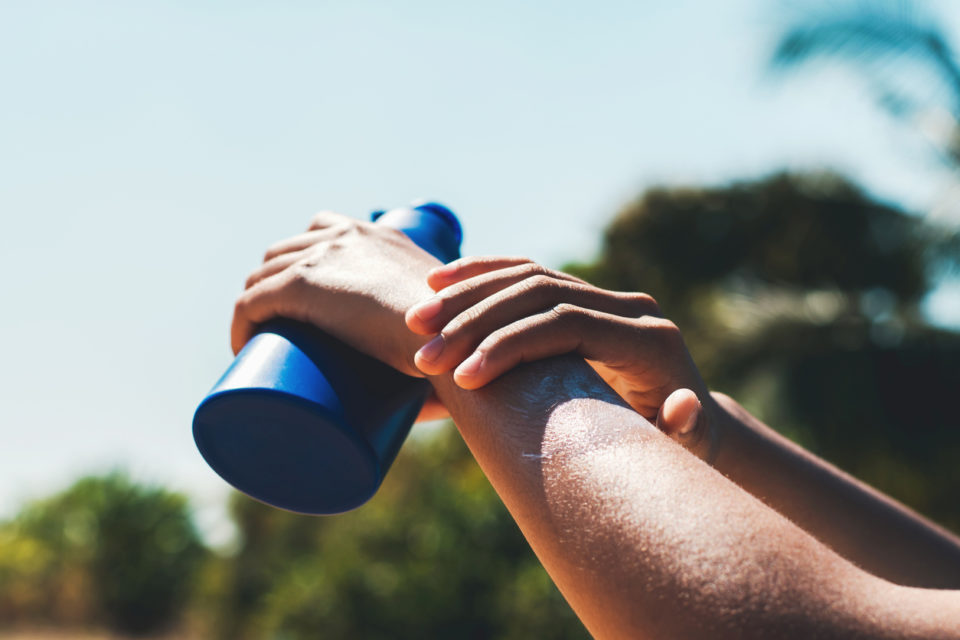 close up of woman applying sunscreen lotion on hand with blue sky background