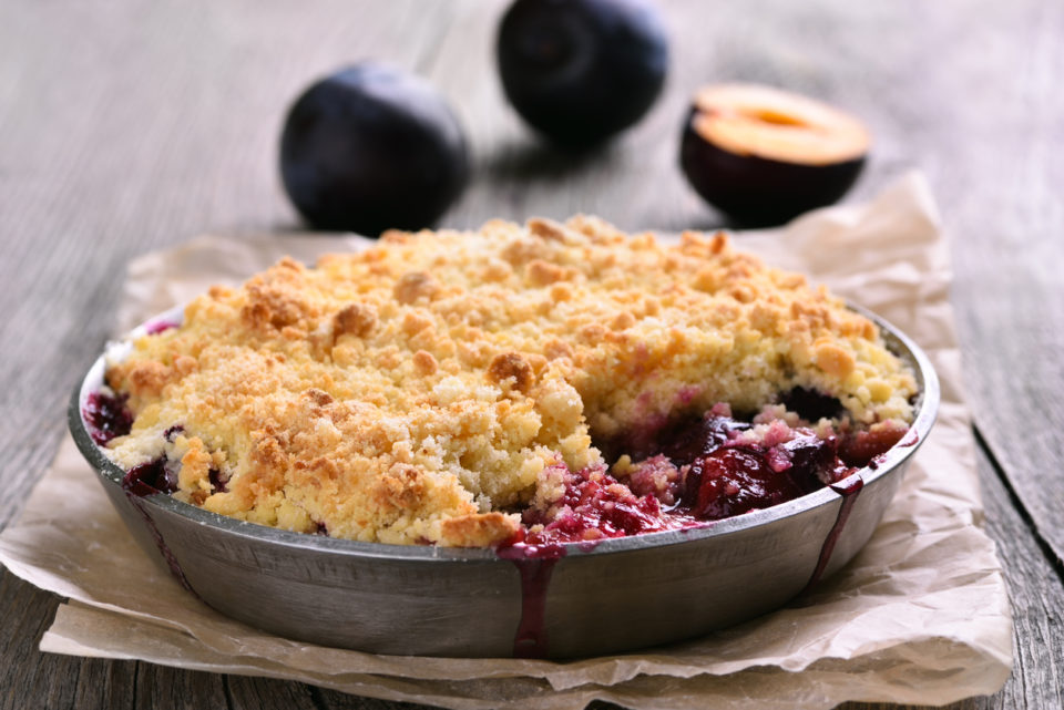 Plum crumb tart in pan on wooden background