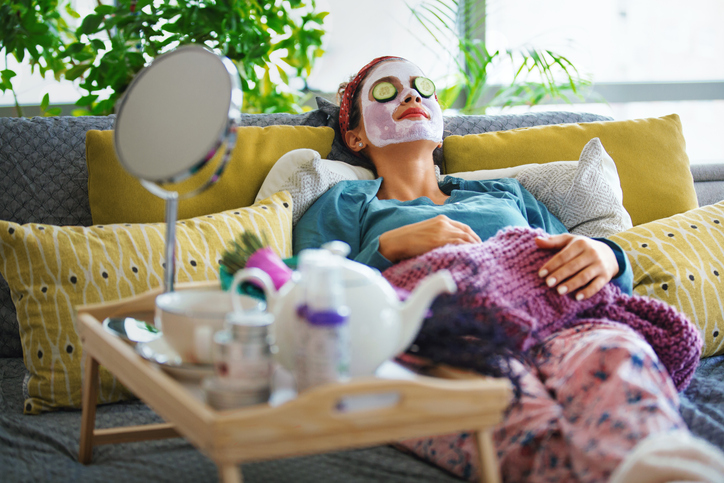 Young woman with a mask and rolls of cucumber on her face is enjoying a morning weekend.