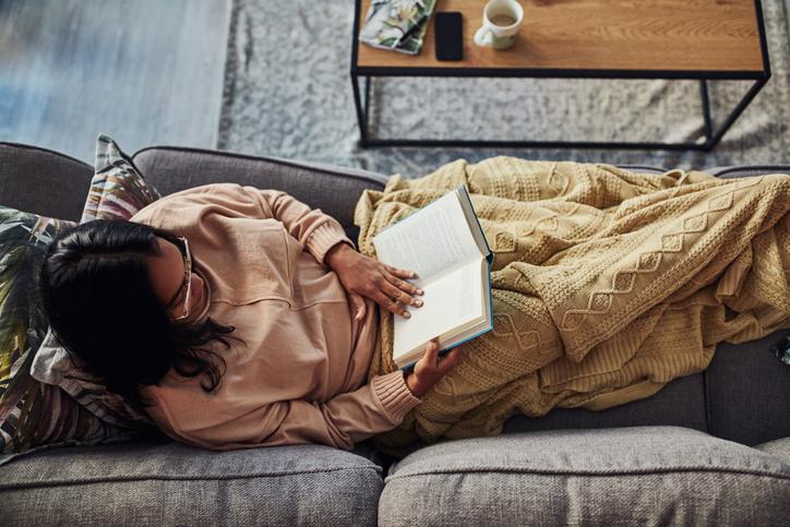 High angle shot of a young woman reading a book on the sofa at home