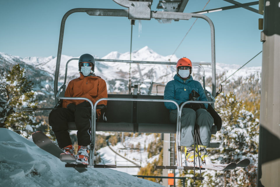 two skiers with mouth nose mask on chair lift