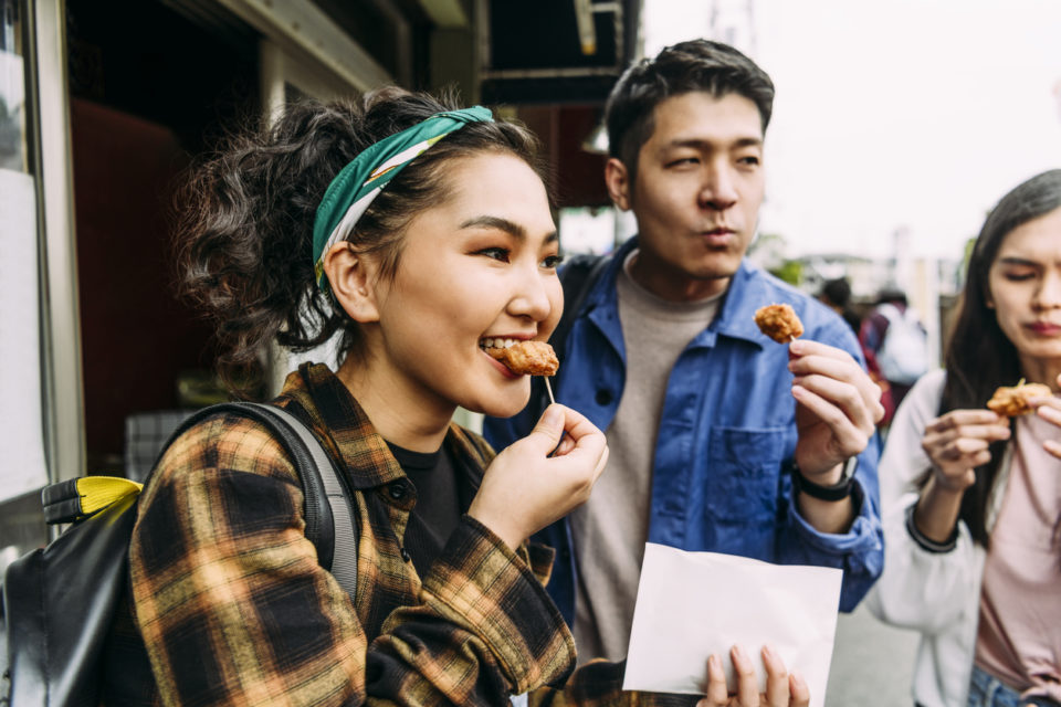 Cheerful young woman eating street food with friends